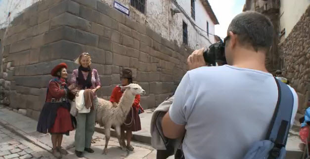 Jóven pareja de turistas tomándose fotos con pobladores en calle empedrada de Cusco